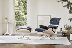 an eames chair and ottoman in front of a window with potted plants on the floor