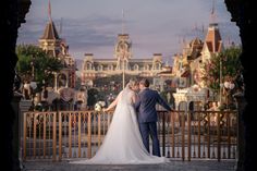 a bride and groom standing on a bridge in front of the disneyland theme park castle