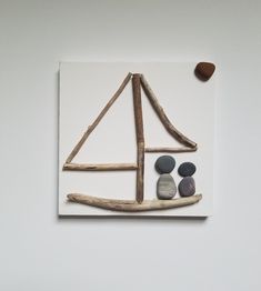 a sailboat made out of driftwood and rocks on a white surface with two pebbles