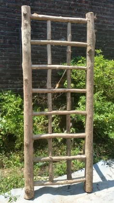 an old wooden ladder leaning against a brick wall in front of some bushes and shrubbery