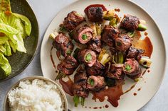 a plate with meat and vegetables on it next to a bowl of rice, salad