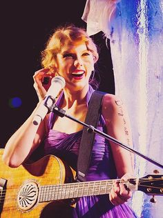 a woman singing into a microphone while holding a guitar