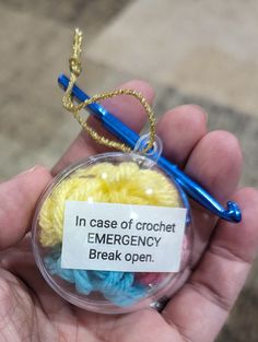 a hand holding a glass ornament with a crochet emergency break open tag on it