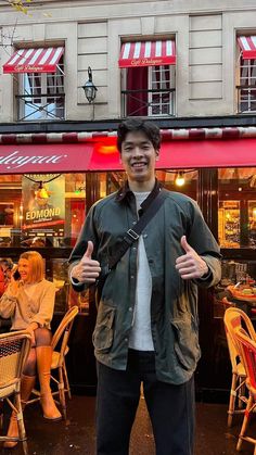 a man standing in front of a restaurant giving the thumbs up sign with his hands