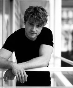 black and white photo of a man leaning on a railing with his arms crossed looking at the camera