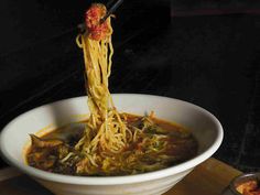 someone is eating noodles with chopsticks in a white bowl on a wooden table