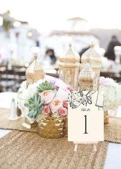 a table topped with vases filled with white and pink flowers next to gold lanterns