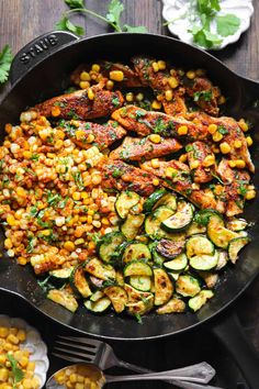 a skillet filled with chicken, zucchini and corn