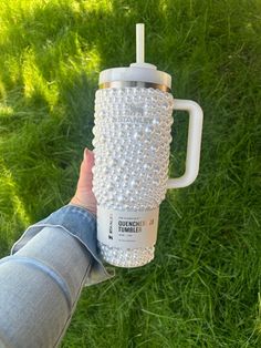 a person holding a coffee cup in their hand on the grass with green grass behind them