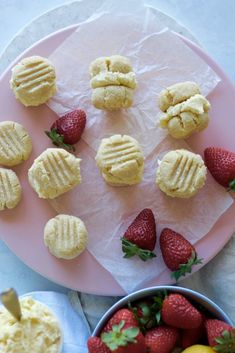 some cookies and strawberries on a pink plate next to a bowl of lemons