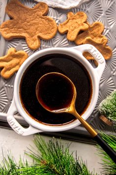 a cup of coffee and some cookies on a tray next to christmas tree branches, with a spoon in it