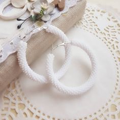 two white beaded hoop earrings sitting on top of a doily next to a piece of fabric