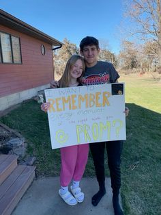 two people standing in front of a house holding a sign that says, we are remember