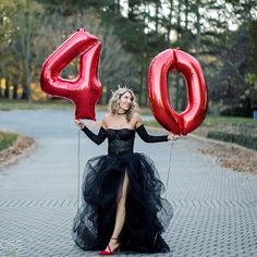 a woman in a black dress holding red balloons that spell out the number forty four