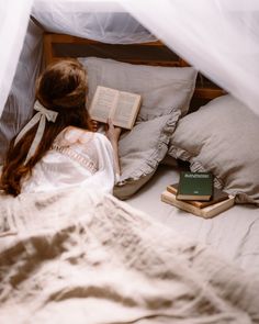 a woman laying in bed reading a book with her head turned to the side and holding an open book