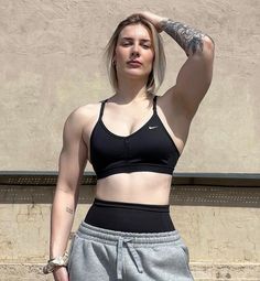 a woman with tattoos standing in front of a building wearing grey sweatpants and a black sports bra top