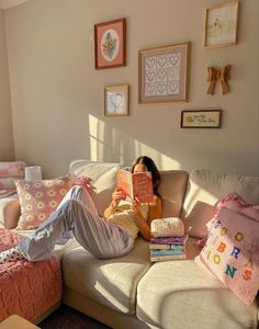 a woman sitting on a couch reading a book in her living room with pink and white decor