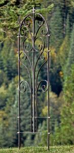 a wrought iron garden trellis in the middle of a grassy field with trees in the background