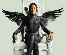 a woman sitting on top of a white chair with black wings over her head and legs