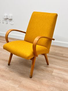 a yellow chair sitting on top of a hard wood floor next to a white wall