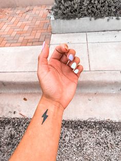 a woman's hand with a small lightning tattoo on her left wrist and pink nail polish