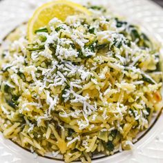 a white plate topped with pasta covered in parmesan cheese and lemon wedges