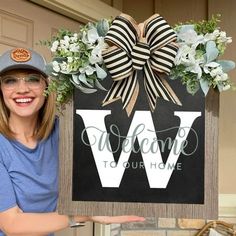 a woman holding up a sign that says welcome to our home with a bow on it