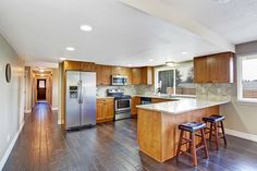 an empty kitchen with wooden floors and stainless steel appliances in the center, along with two bar stools