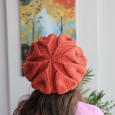 a woman with long hair wearing an orange knitted hat in front of a painting