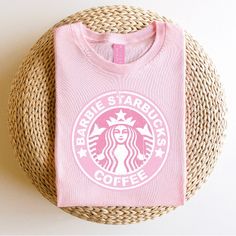 a pink starbucks t - shirt sitting on top of a basket next to a straw bag