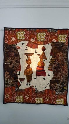 a quilt hanging on the wall with two people holding an umbrella and another person standing next to it