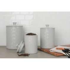 three white kitchen canisters sitting on top of a counter next to utensils