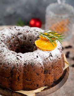 a bundt cake with orange slices and rosemary sprigs on top, sitting on a wooden platter