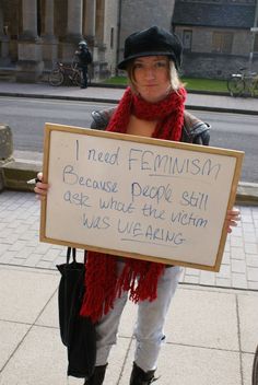 a woman holding a sign that says i need feminist because people still get what the victim is wearing