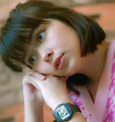 a young woman with her hand on her chin looking at the camera while wearing a watch