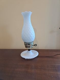 a white glass vase sitting on top of a wooden table next to a light bulb