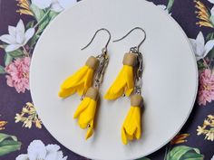 two pairs of yellow and brown earrings on a white plate with flowers in the background