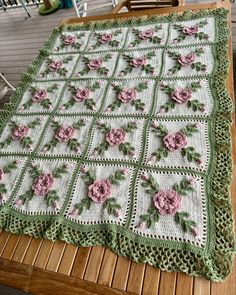 a crocheted blanket with pink flowers on it sitting on a wooden table next to a chair