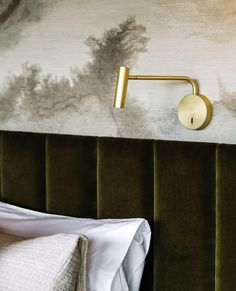 a bed with a green velvet headboard and gold metal wall light on the side