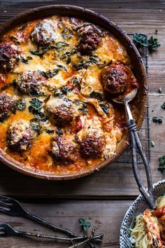 a bowl of pasta with meatballs and spinach on the side next to two serving spoons