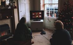 two people sitting in front of a christmas tree watching tv