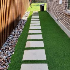 a walkway made out of stepping stones in the grass next to a brick wall and fence