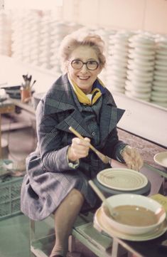 an older woman sitting on a table with bowls and spoons