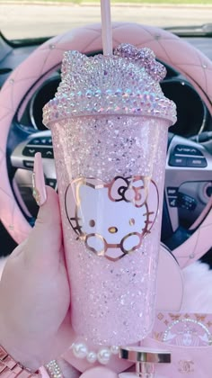 a person holding up a pink hello kitty cup in their hand and steering wheel behind her