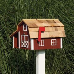 a red and white mailbox with a house on it's roof in front of some tall grass