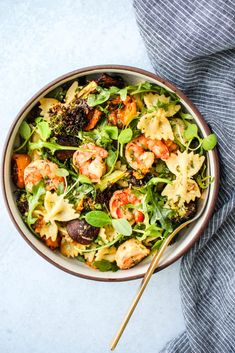 a bowl filled with pasta and shrimp on top of a blue table cloth next to a wooden spoon