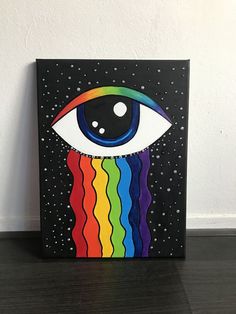 an eye painted on a black canvas with rainbow stripes in the bottom and white dots above it