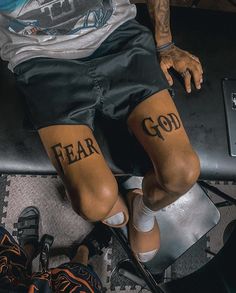 a man sitting on top of a metal bench with his feet covered in tattoos that say fear and god