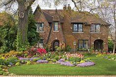 a large brick house with lots of flowers in the front yard and landscaping around it