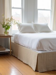 a bed with white sheets and pillows in a bedroom next to a window filled with curtains